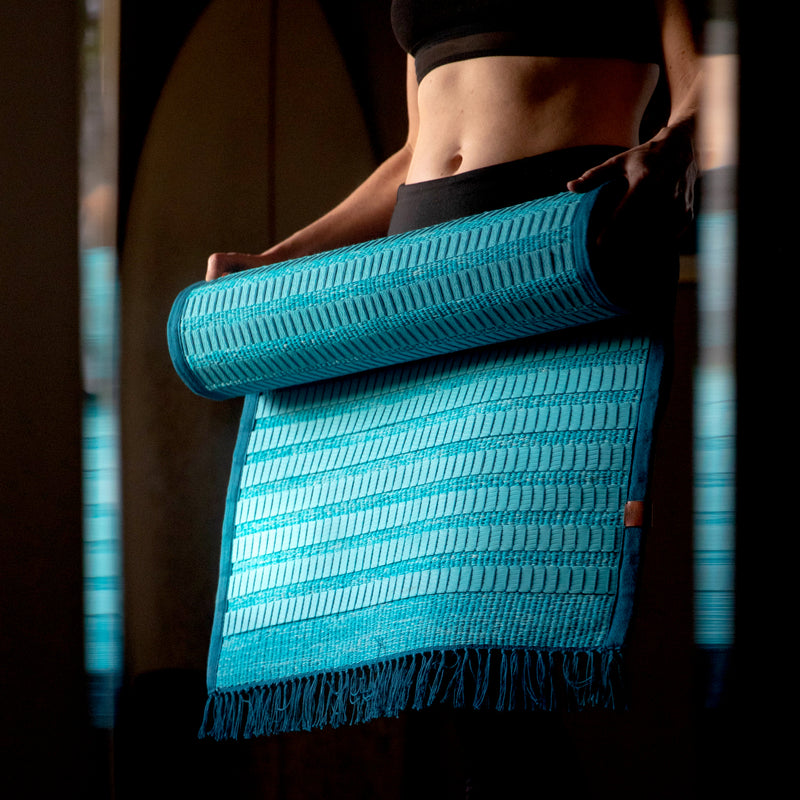 woman holding handwoven, organic hemp, non-toxic foam turquoise Ritual Rug yoga mat in front of mirror