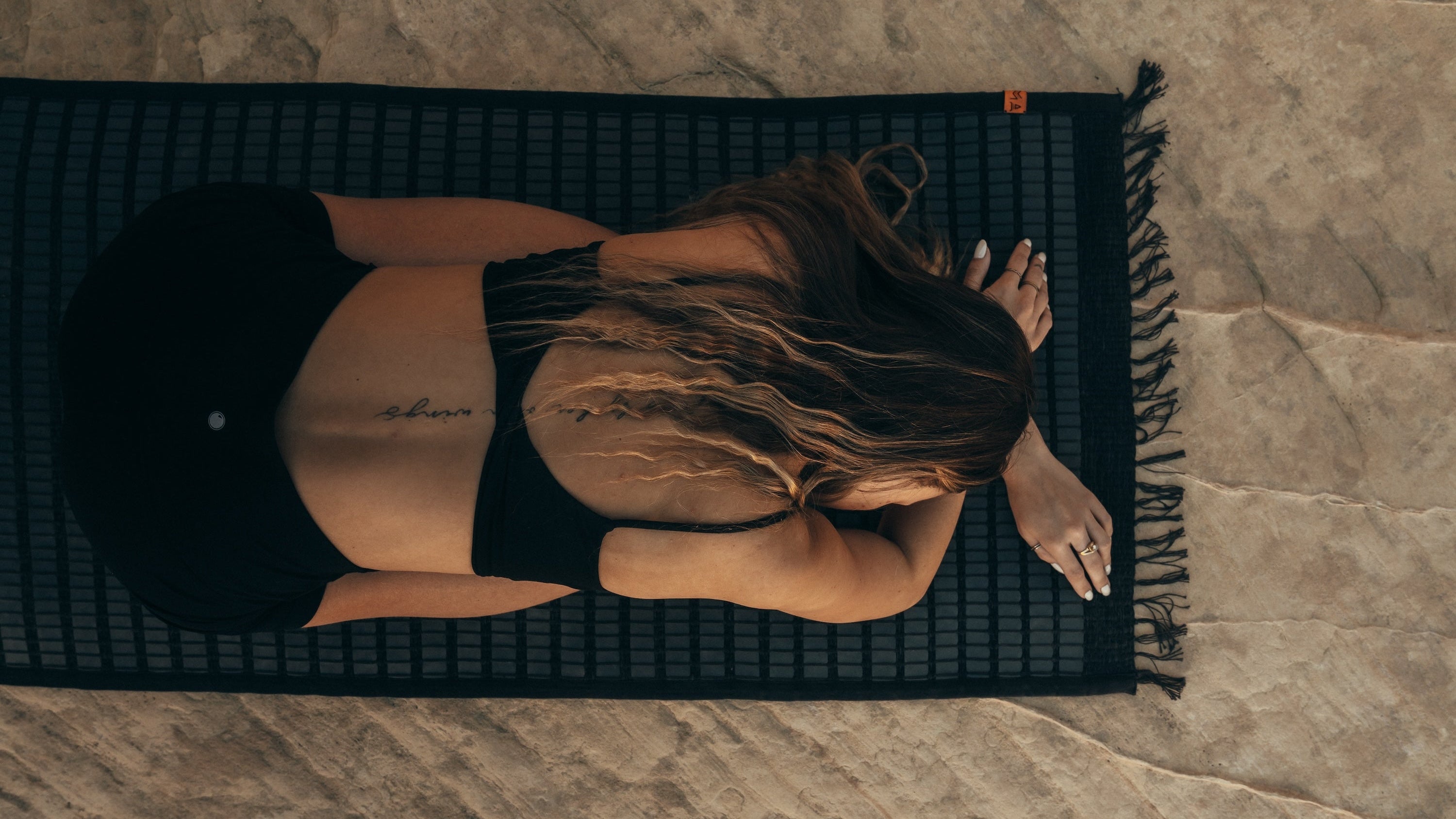 Person lying on a black yoga mat on a stone floor